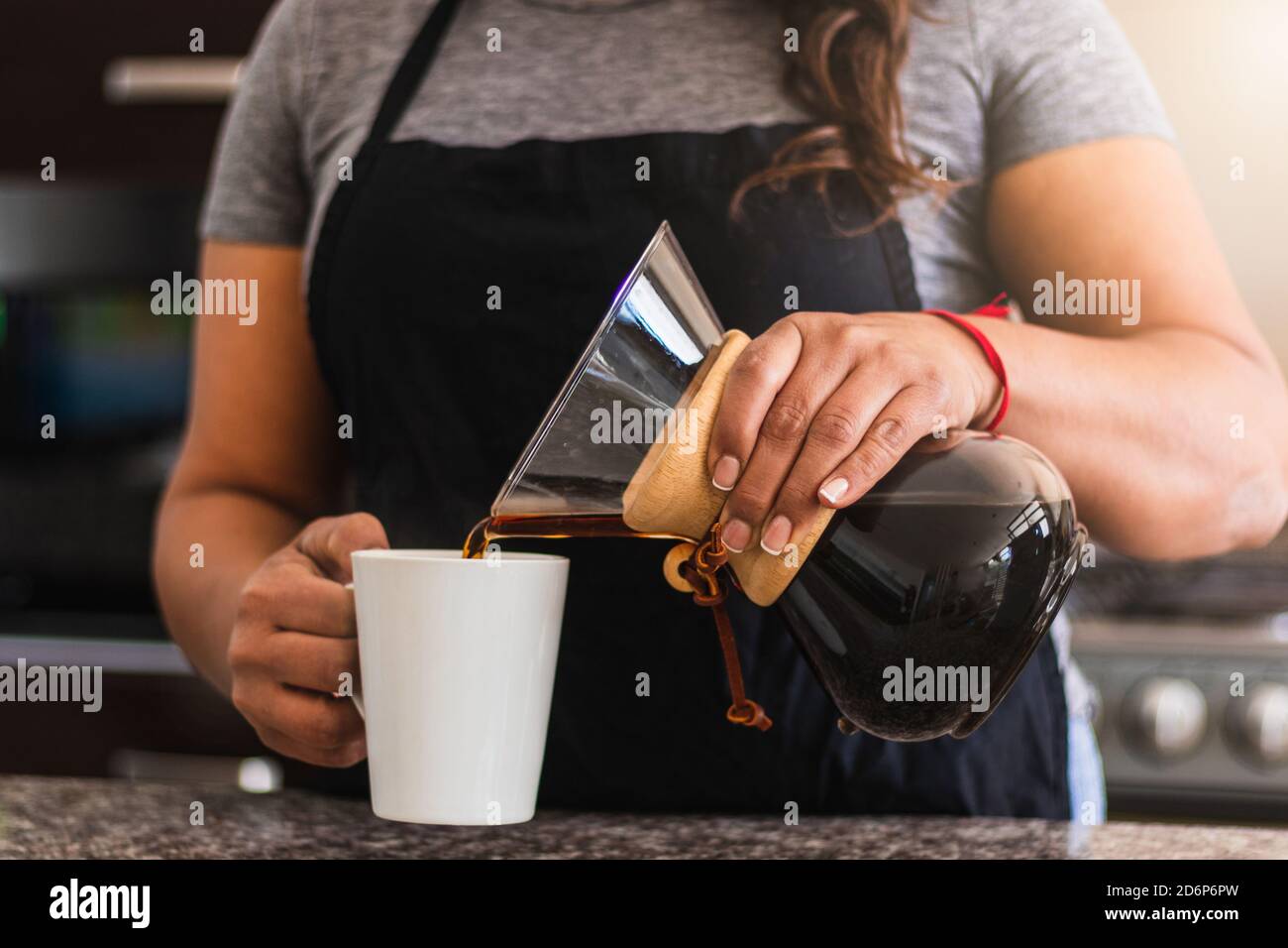 Hispanische Barista gießt Kaffee in eine weiße Tasse in der Familienküche. Schwarze Frau hält gießen über Kaffeekanne am Morgen Stockfoto