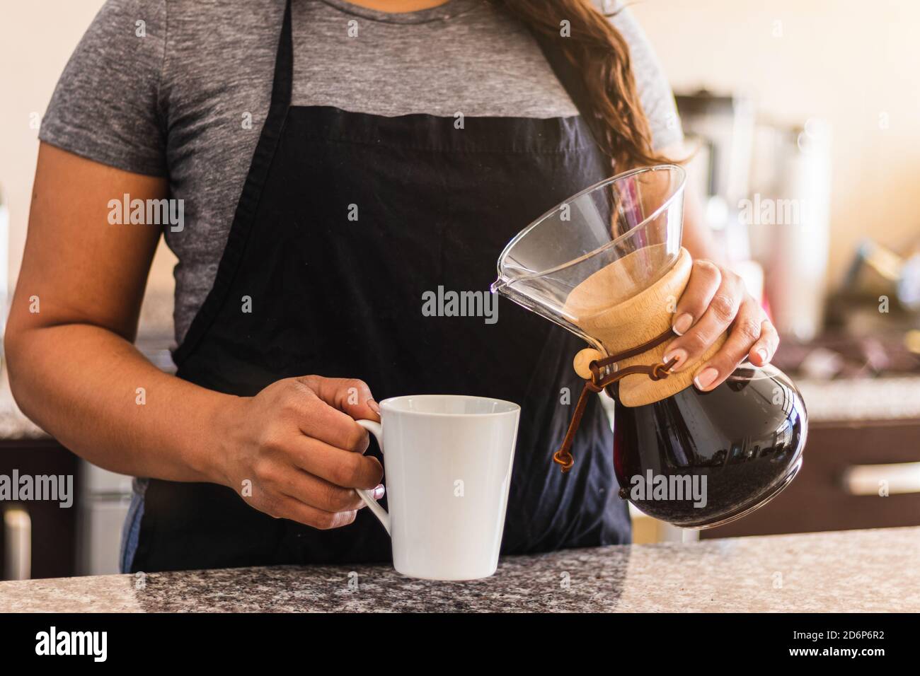 Hispanische Barista gießt Kaffee in eine weiße Tasse in der Familienküche. Schwarze Frau hält gießen über Kaffeekanne am Morgen Stockfoto