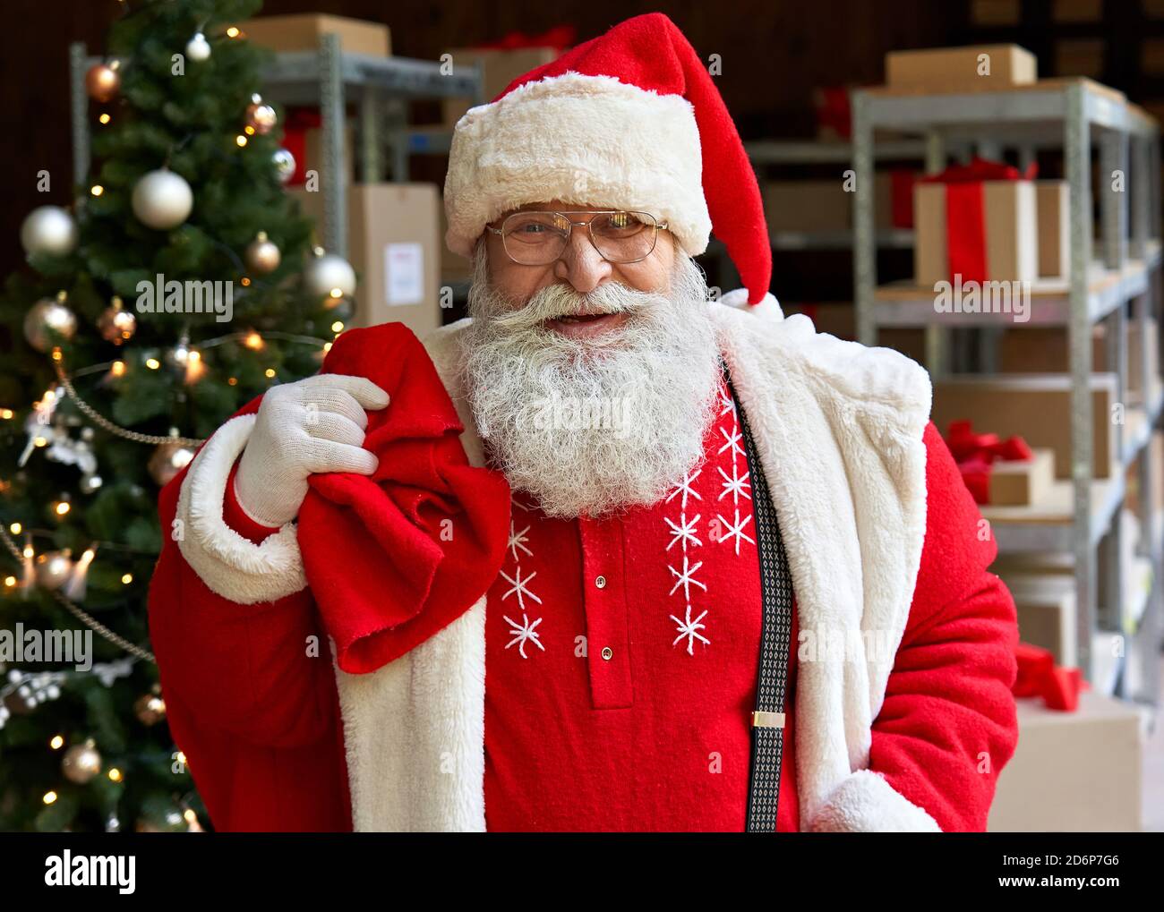 Happy Santa Claus trägt Kostüm mit Sack Tasche mit Geschenken in der Werkstatt. Stockfoto