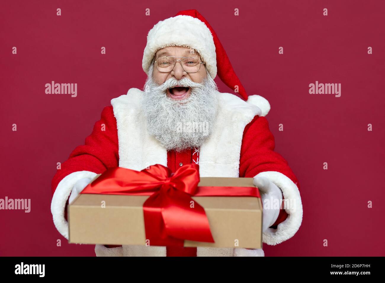 Glücklicher Weihnachtsmann hält präsent, lachend, auf rotem Hintergrund stehend. Stockfoto