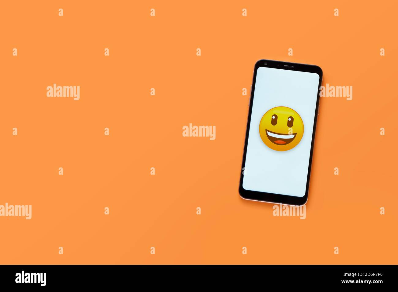 Draufsicht auf Handy mit lächelndem Gesicht Emoticon auf weißem Bildschirm. Minimalistisches Design, orangefarbener Hintergrund, Kopierbereich. Konzept für soziale Netzwerke. Stockfoto