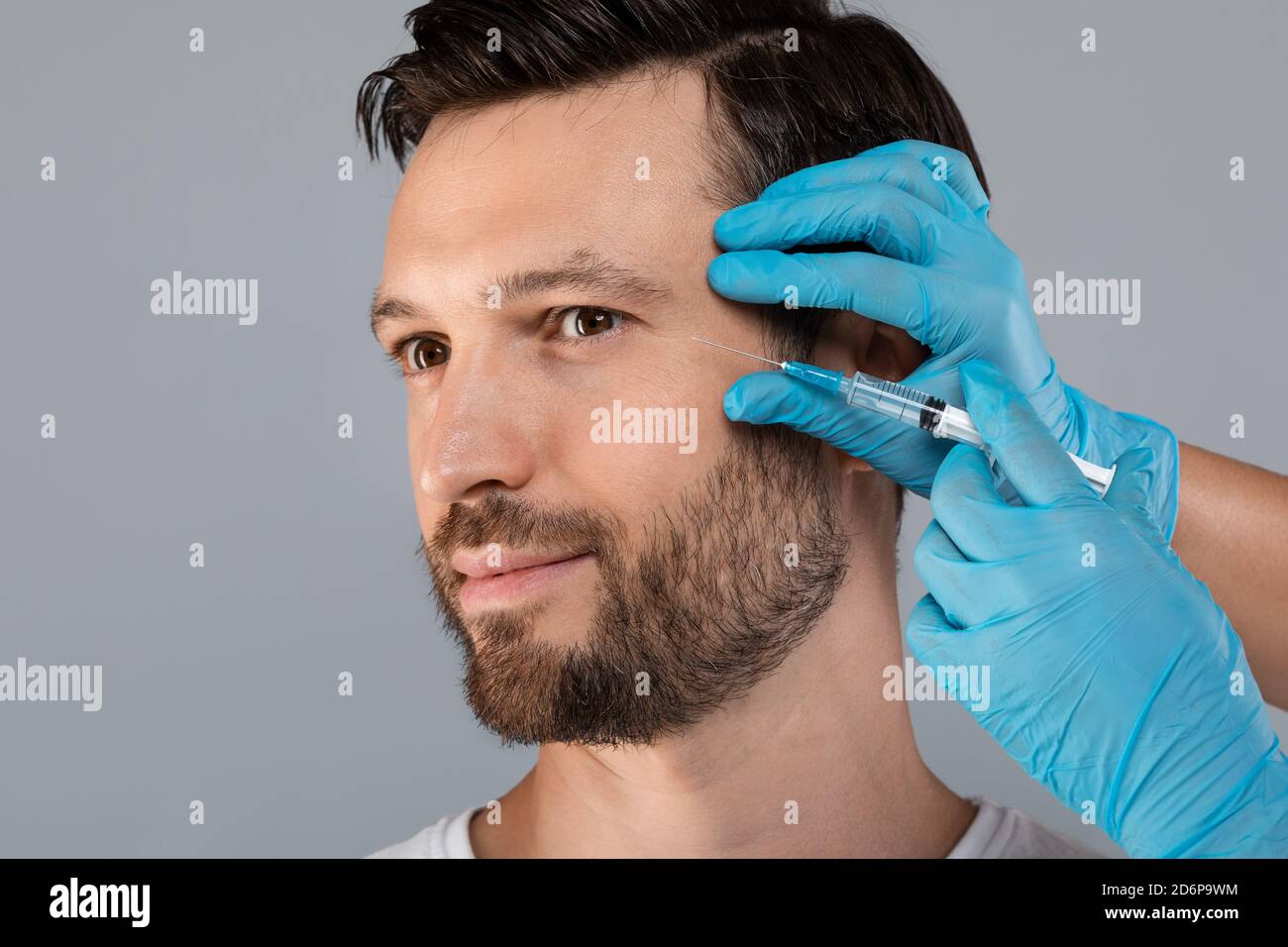 Plastischer Chirurg injiziert Gesichtsfüller für Mann mittleren Alters, leerer Raum Stockfoto