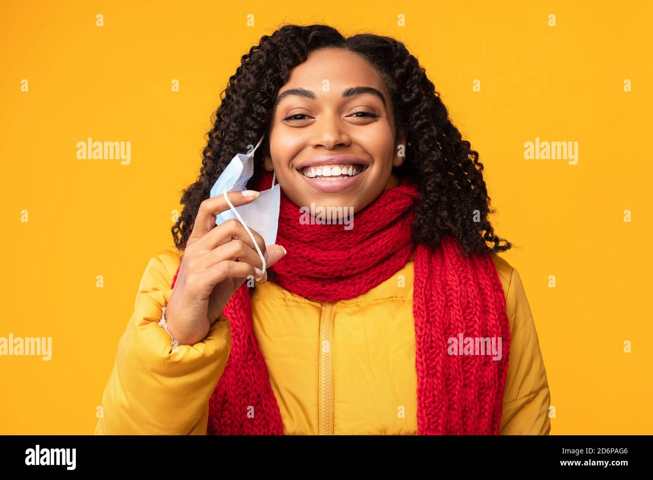 Happy African Lady Abheben Schützende Gesichtsmaske, Gelber Hintergrund Stockfoto
