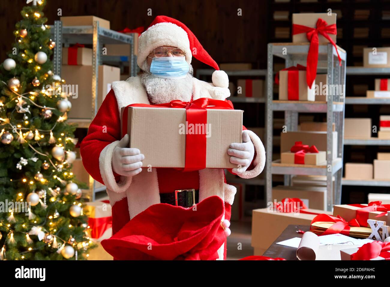 Weihnachtsmann trägt Kostüm Gesichtsmaske hält Weihnachtsgeschenke in der Werkstatt. Stockfoto