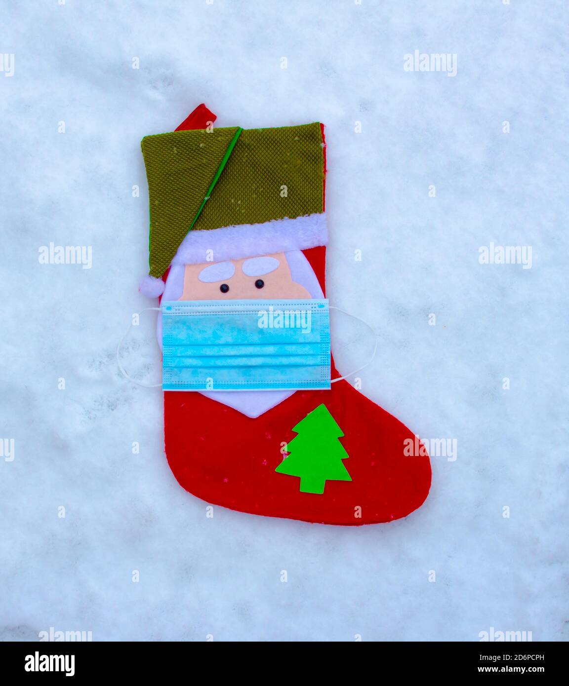 Eine weihnachtliche Socke Ornament Dekoration mit einer Gesichtsmaske auf Schnee. Konzept: Covid-19, Coronavirus während der Weihnachtszeit. Stockfoto