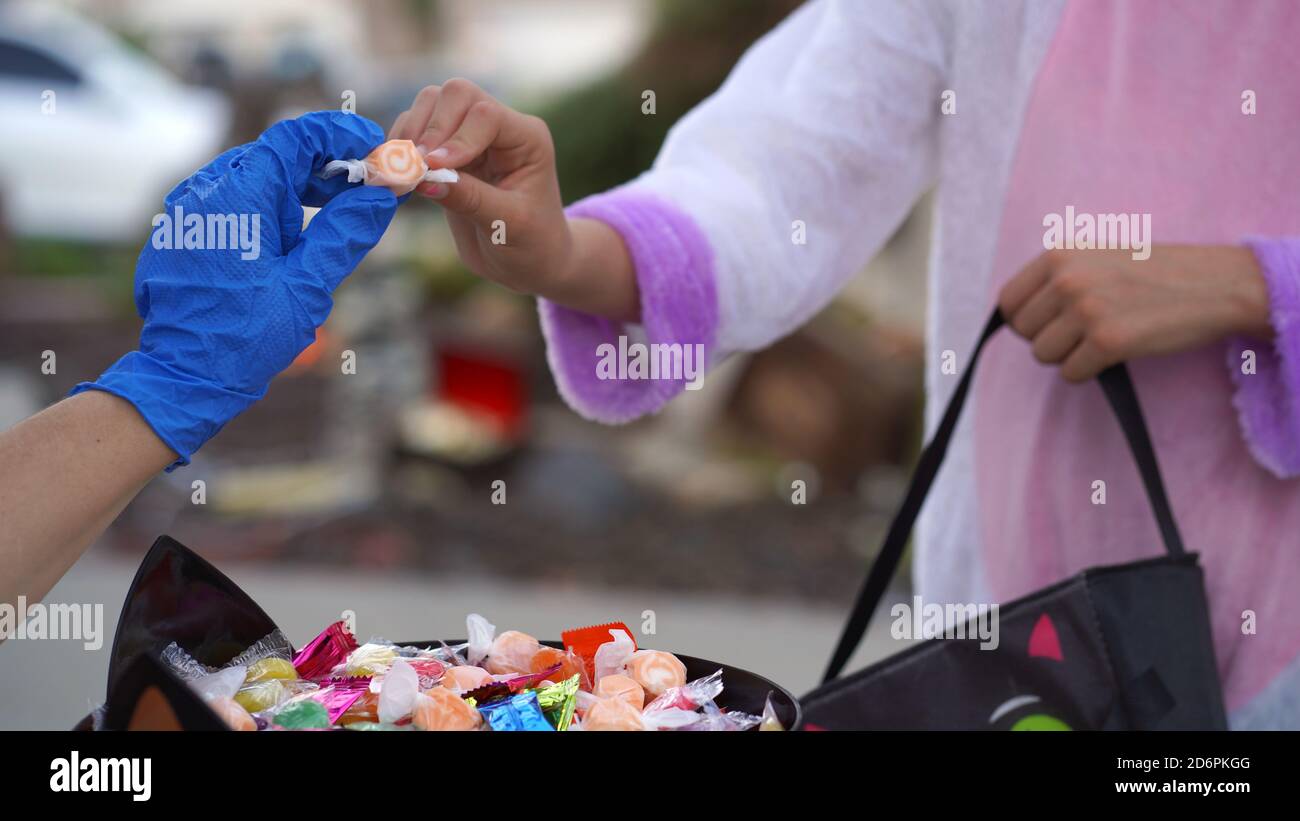Halloween 2020: Nahaufnahme einer Hand mit Handschuhen, die Süßigkeiten an ein junges Mädchen in einem Kostüm ausgibt Stockfoto
