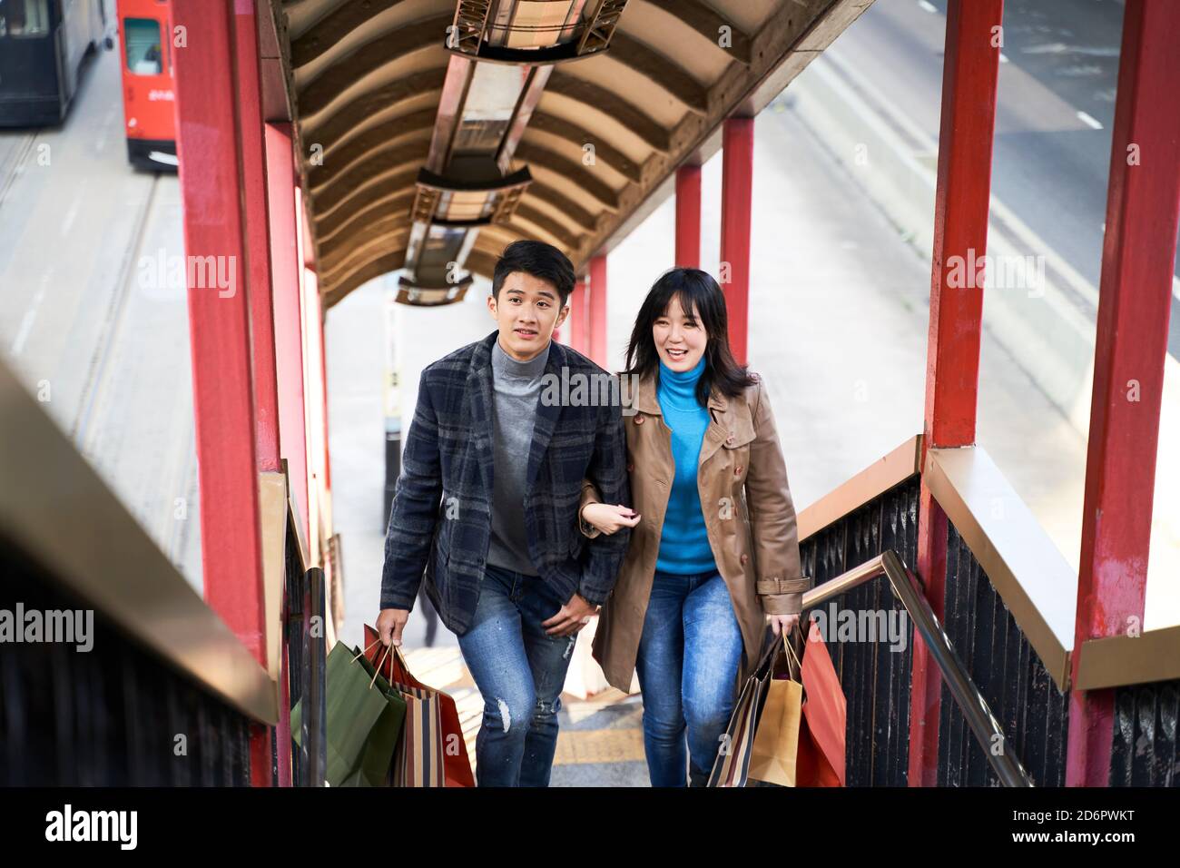 Junges asiatisches Paar, das Einkaufstüten hält, die eine Fußgängerüberführung aufsteigen Stockfoto