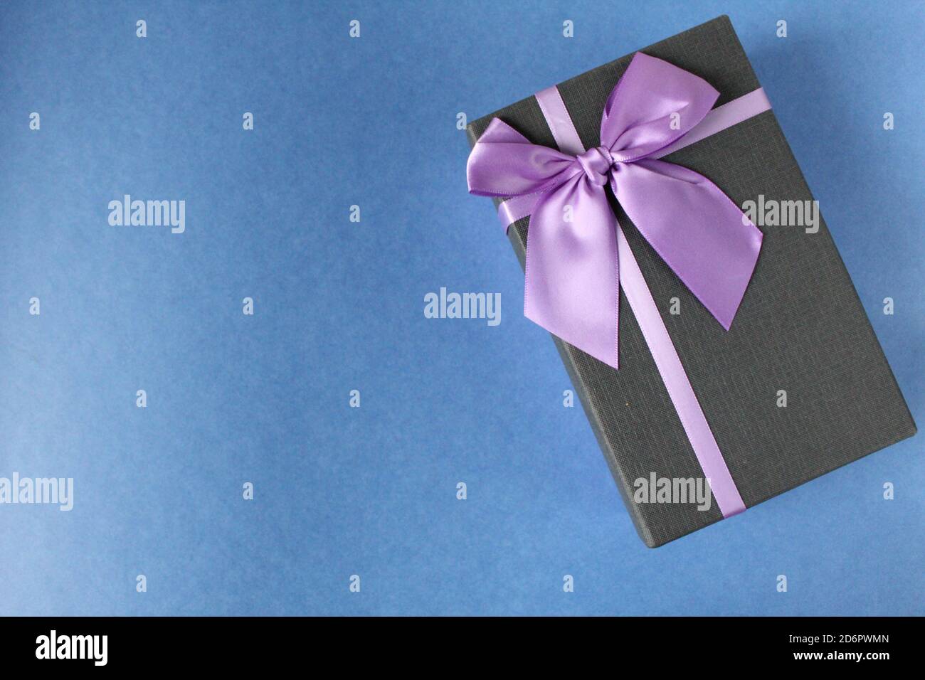 Geschenk in einer schwarzen Box und lila lila Flieder und Bogen für den Urlaub Neujahr Weihnachten Muttertag Geburtstag Firmenfeier auf blauem Hintergrund mit Stockfoto