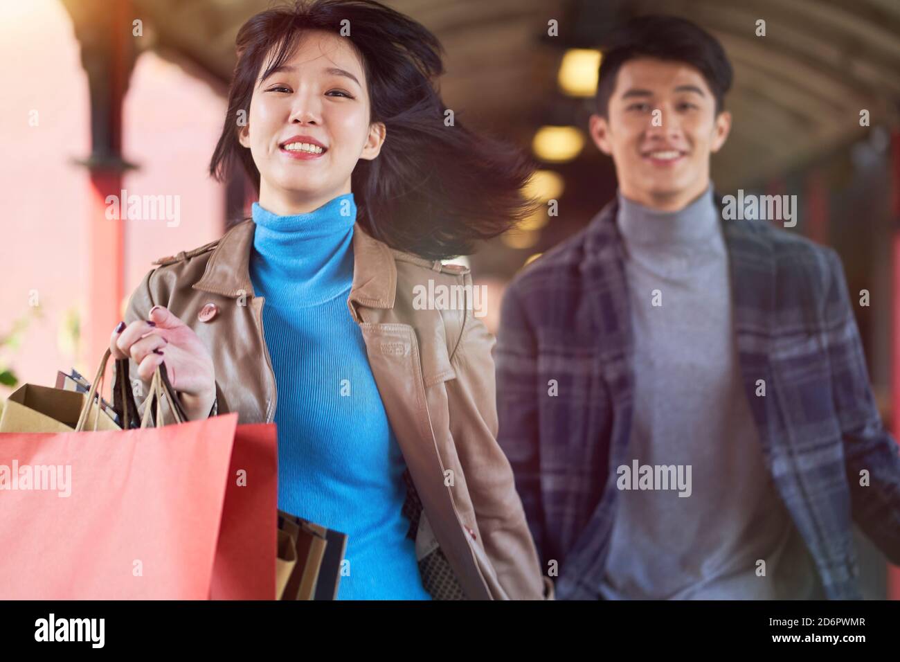 Junge asiatische Paar läuft auf Fußgängerüberführung mit Einkaufstaschen In den Händen glücklich und lächelnd Stockfoto