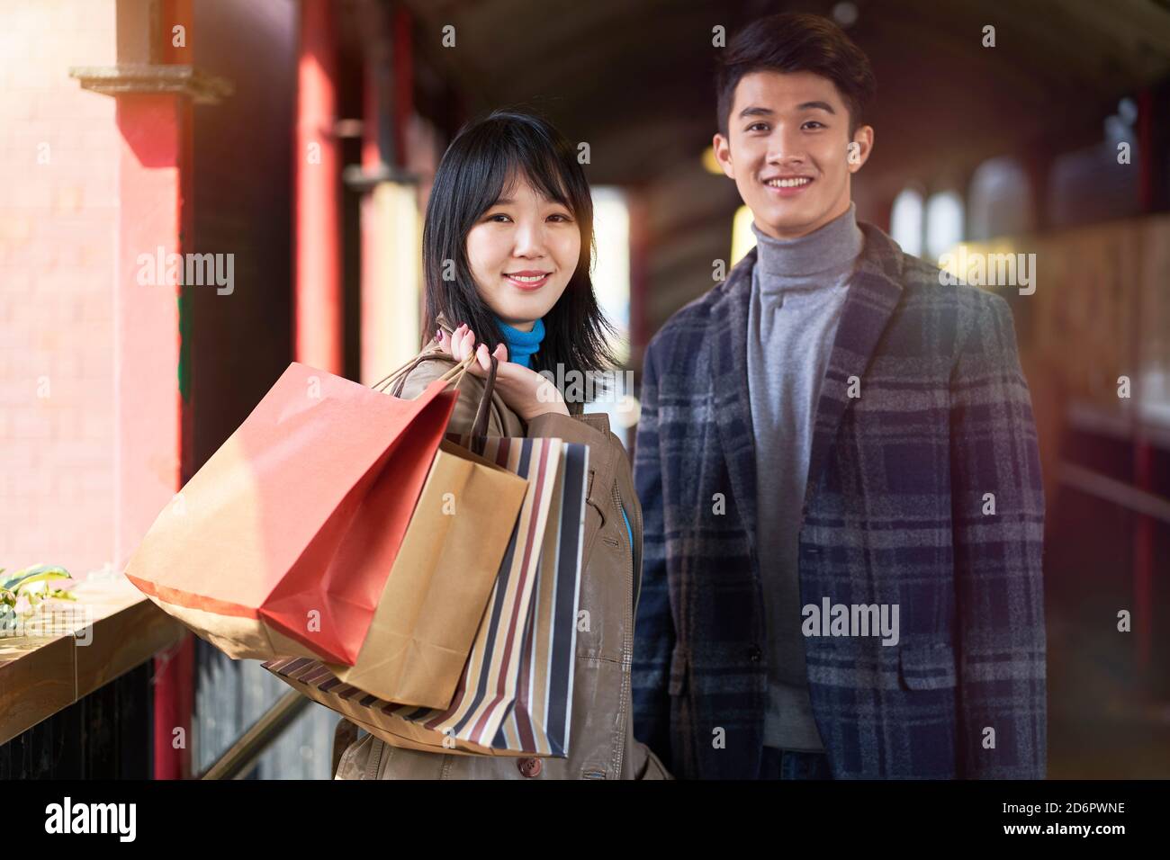 Junge liebende asiatische Paar auf einem Fußgängerüberführung halten stehen Einkaufstaschen blicken lächelnd auf die Kamera Stockfoto