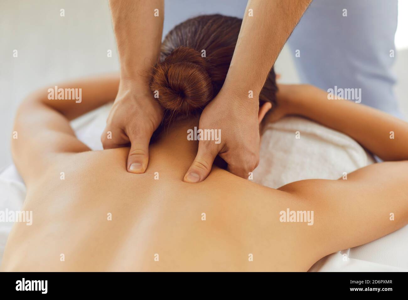 Männerhände machen eine therapeutische Nackenmassage für ein Mädchen, das auf einer Massagescouch in einem Massage-Spa liegt. Stockfoto