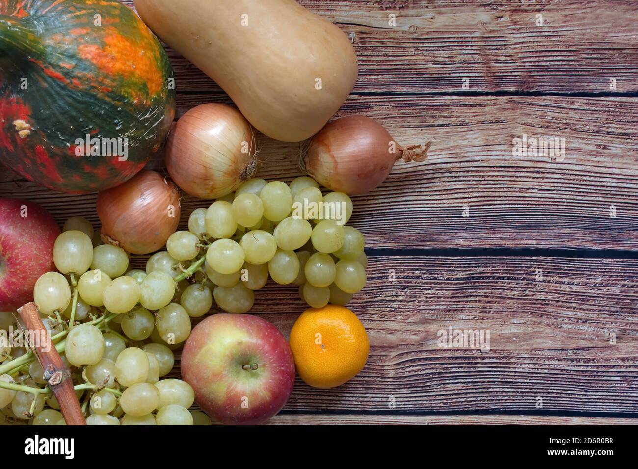 Herbstkomposition mit Kürbis, Zwiebel, Apfel, Mandarine und Trauben auf Holzgrund Stockfoto