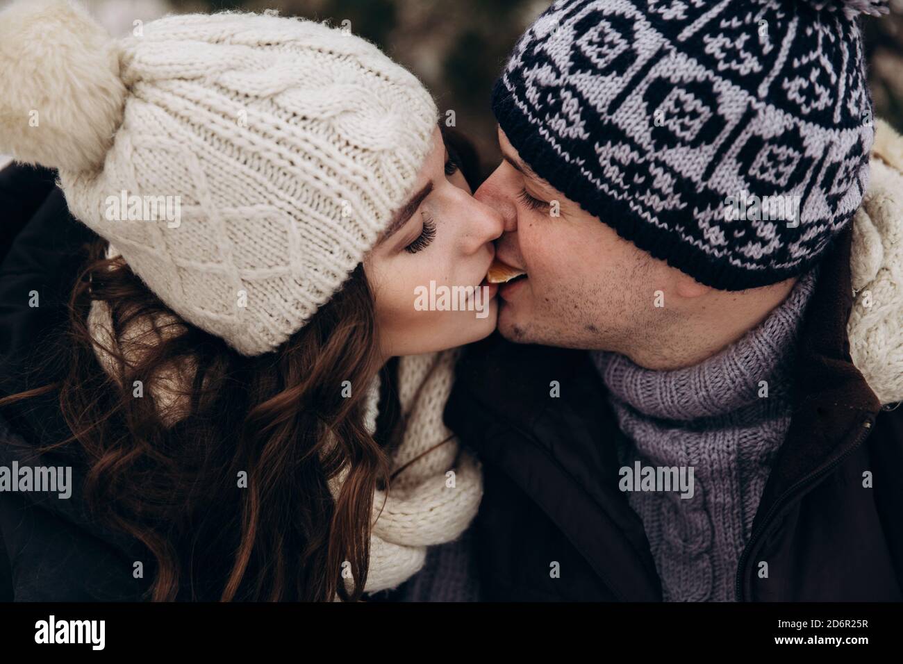 Junge schöne Paar essen Mandarine und küssen in Wintermützen Und Jacken Stockfoto