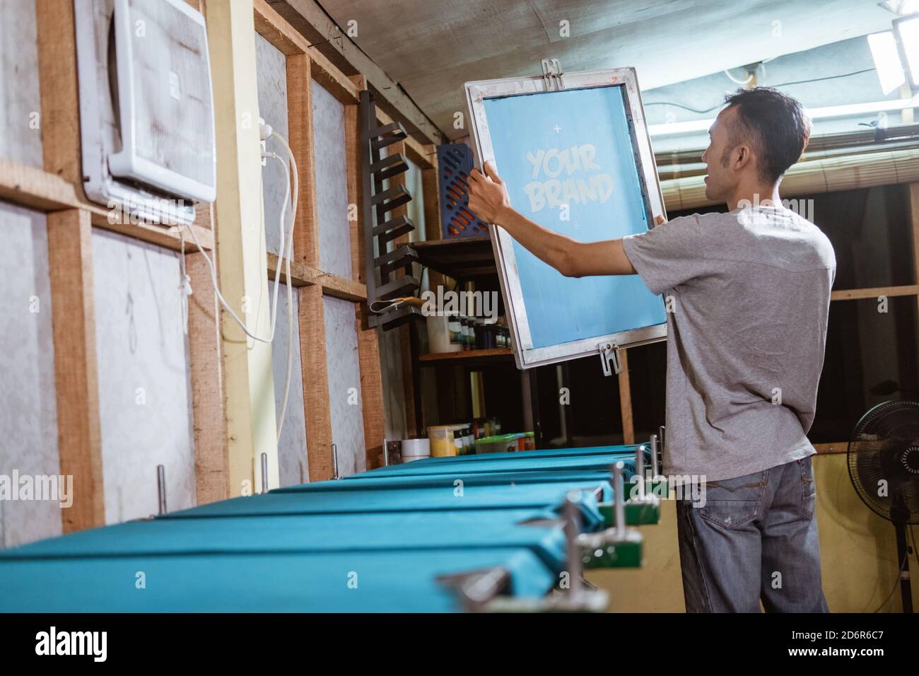 Männlicher Arbeiter hält den Siebdruck-Rahmen und beobachtet sorgfältig die Der resultierende Film auf dem Siebdruck vor dem Siebdruck Stockfoto