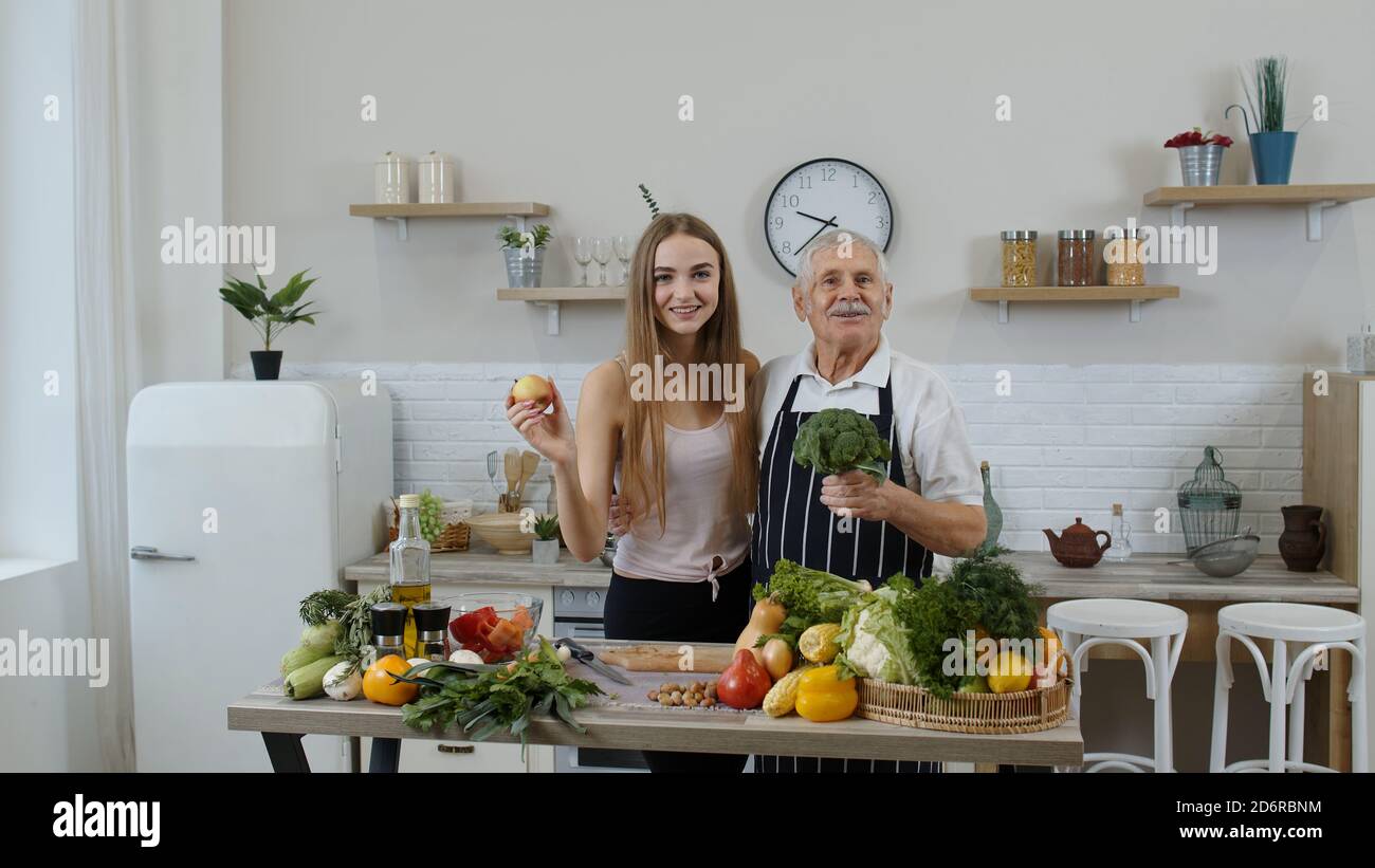 Älterer Großvater mit Enkelin in der Küche. Mädchen mit reifen Mann empfehlen essen rohe Gemüse Lebensmittel. Brokkoli, Apfel. Gesunde pflanzliche Ernährung Diät-Konzept. Welt vegan Tag Stockfoto