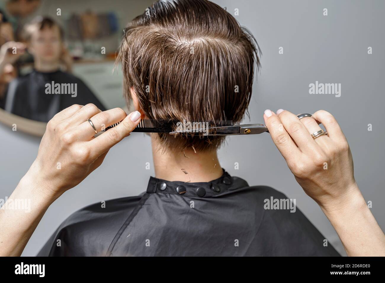 Hair Cutting Prozess. Junge Frau sitzt in Friseurstuhl vor dem Spiegel. Professionelle schneidet Haare für Kunden Stockfoto