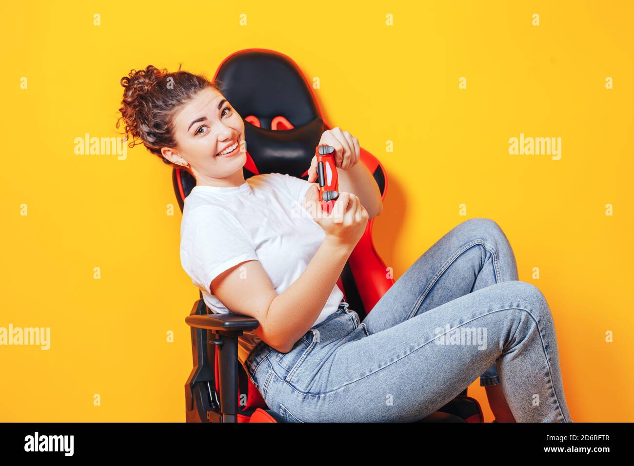 Frau, die hinter einem Spielstuhl in ihren Händen sitzt und rot hält Gamepad auf gelbem Hintergrund Stockfoto