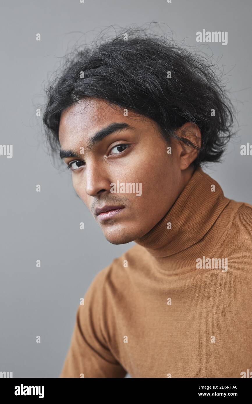 Vertikales Porträt von exotischen jungen Mann der indianischen Erbe Blick auf die Kamera, während posiert vor grauem Hintergrund, einzigartige Schönheit Konzept Stockfoto