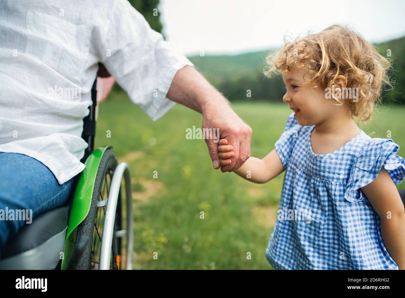 Kleine gir mit unkenntlichen älteren Großvater im Rollstuhl auf einem Spaziergang auf der Wiese in der Natur. Stockfoto