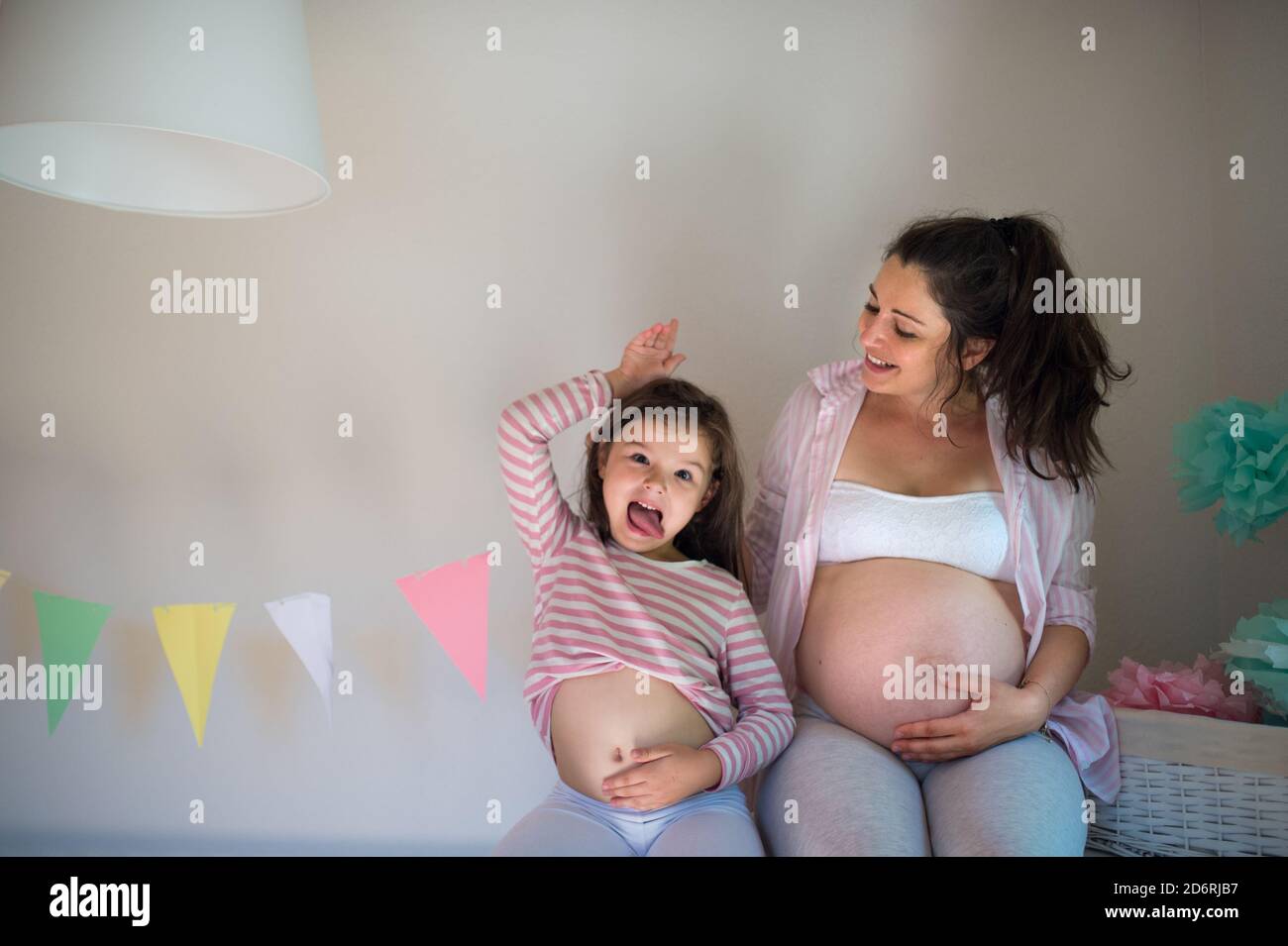 Portrait einer schwangeren Frau mit kleiner Tochter im Haus, zeigt Bauch. Stockfoto