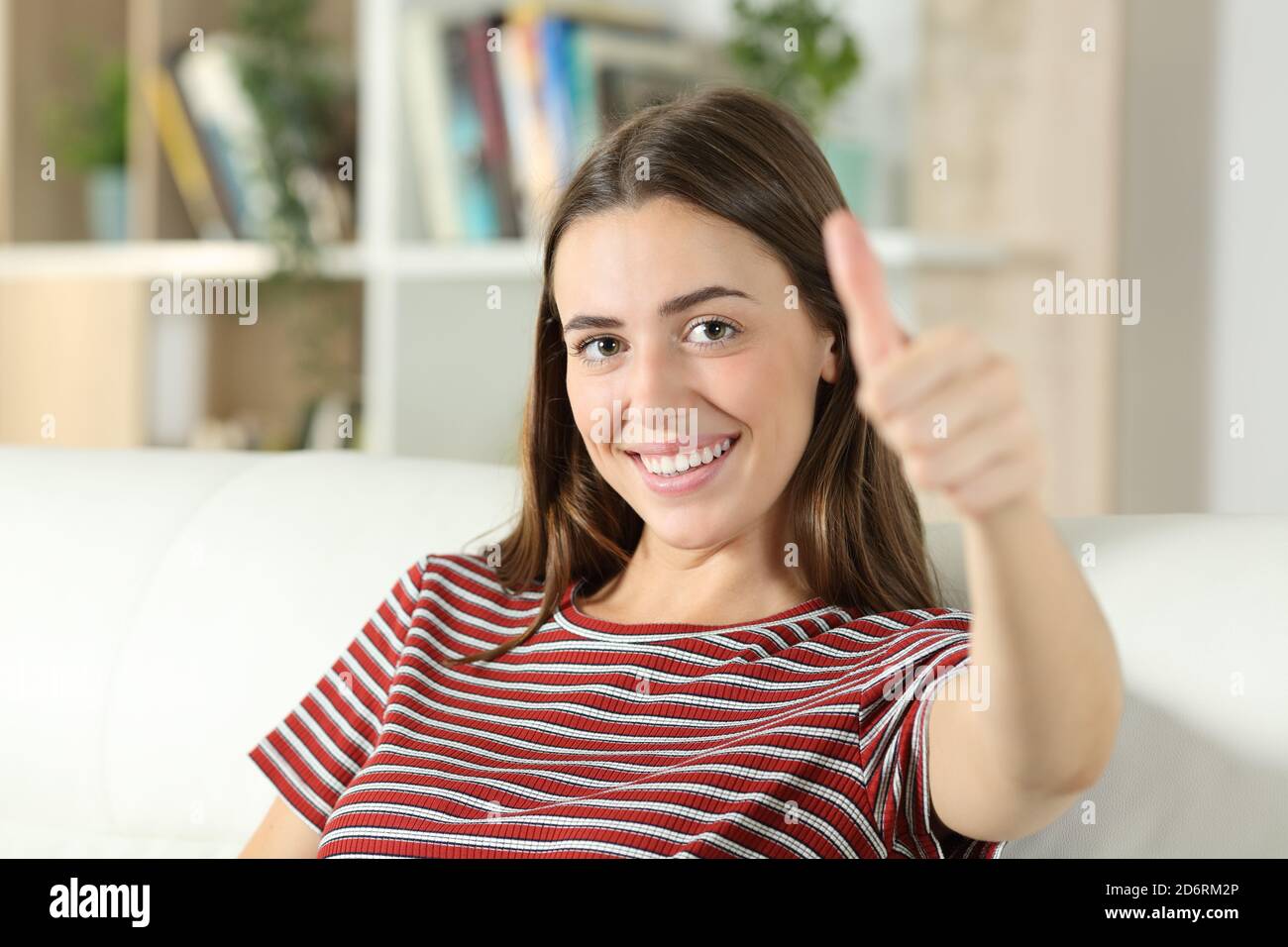 Glückliche Frau lächelt an der Kamera mit dem Daumen nach oben sitzend Eine Couch im Wohnzimmer zu Hause Stockfoto