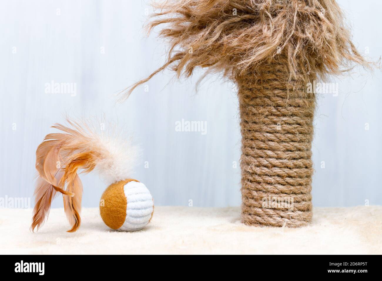 Gebrauchte Katze Kratzpfosten mit zerlumpten Teilen und Katzenspielzeug Runde Kugel mit Federn auf weißem Hintergrund Stockfoto