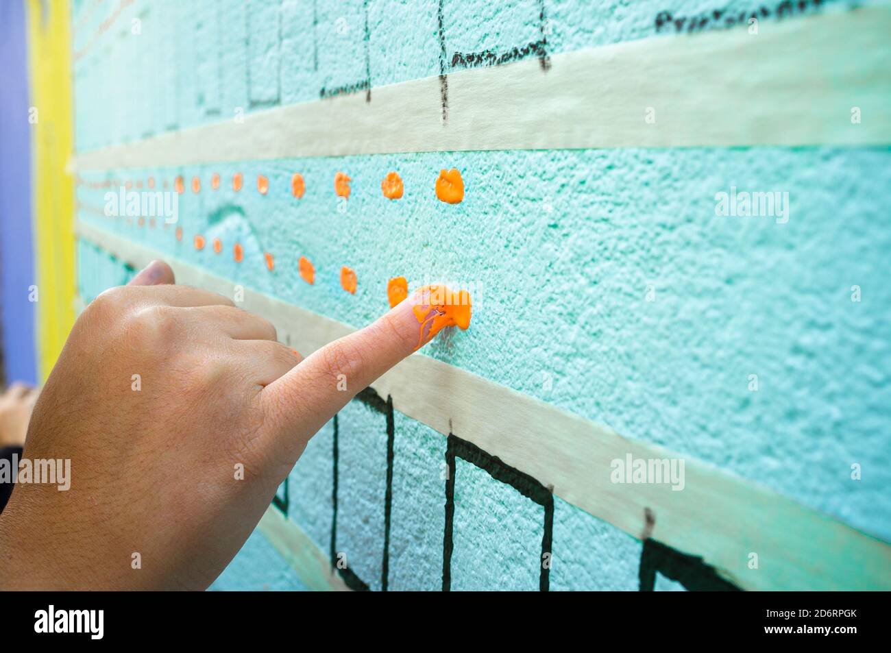 Künstlerin malt Wand mit ihrem kleinen Finger. Zuvor geklebtes Abdeckband Stockfoto