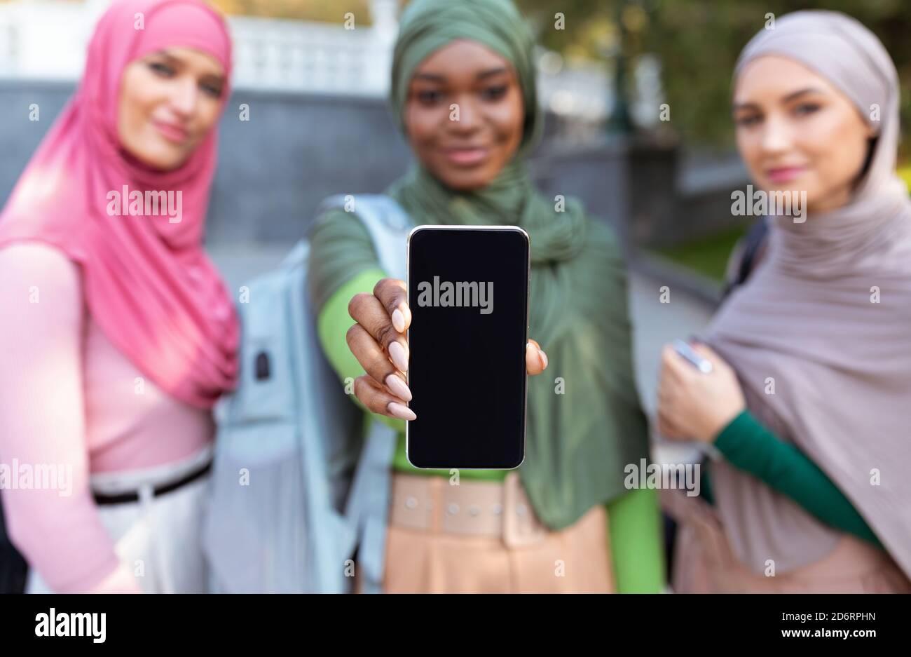 Drei Muslimische Frauen Zeigen Smartphone-Bildschirm Im Freien, Fokus Auf Telefon Stockfoto