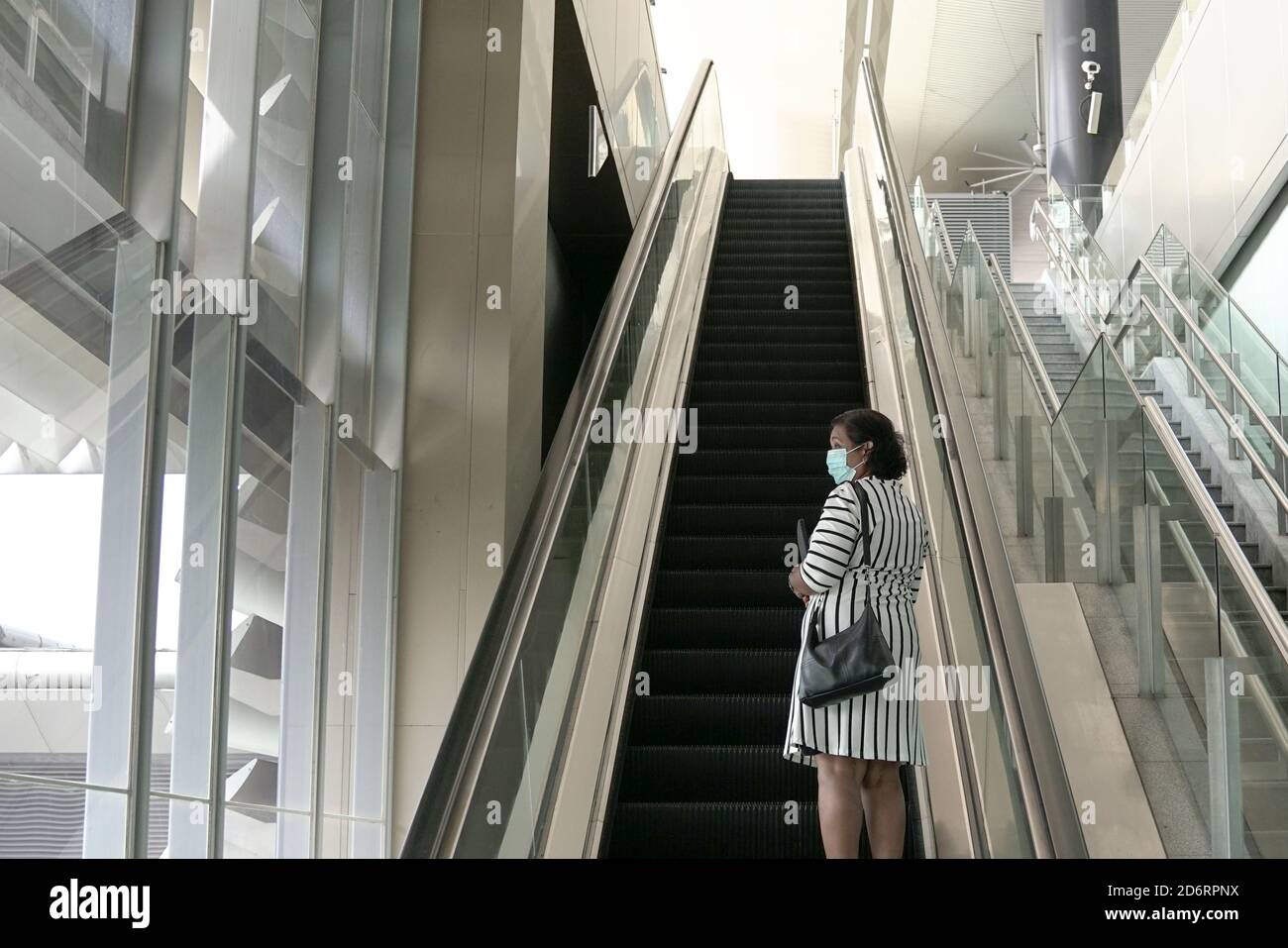 Geschäftsfrau mit Gesichtsmaske auf einer Rolltreppe stehend, nach oben Stockfoto