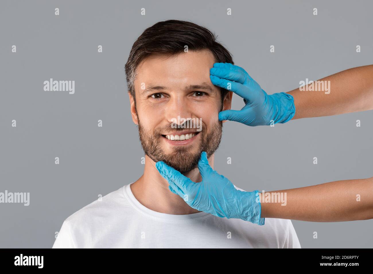Kosmetikerin Hände in Schutzhandschuhen berühren lächelnd Mann Gesicht Stockfoto