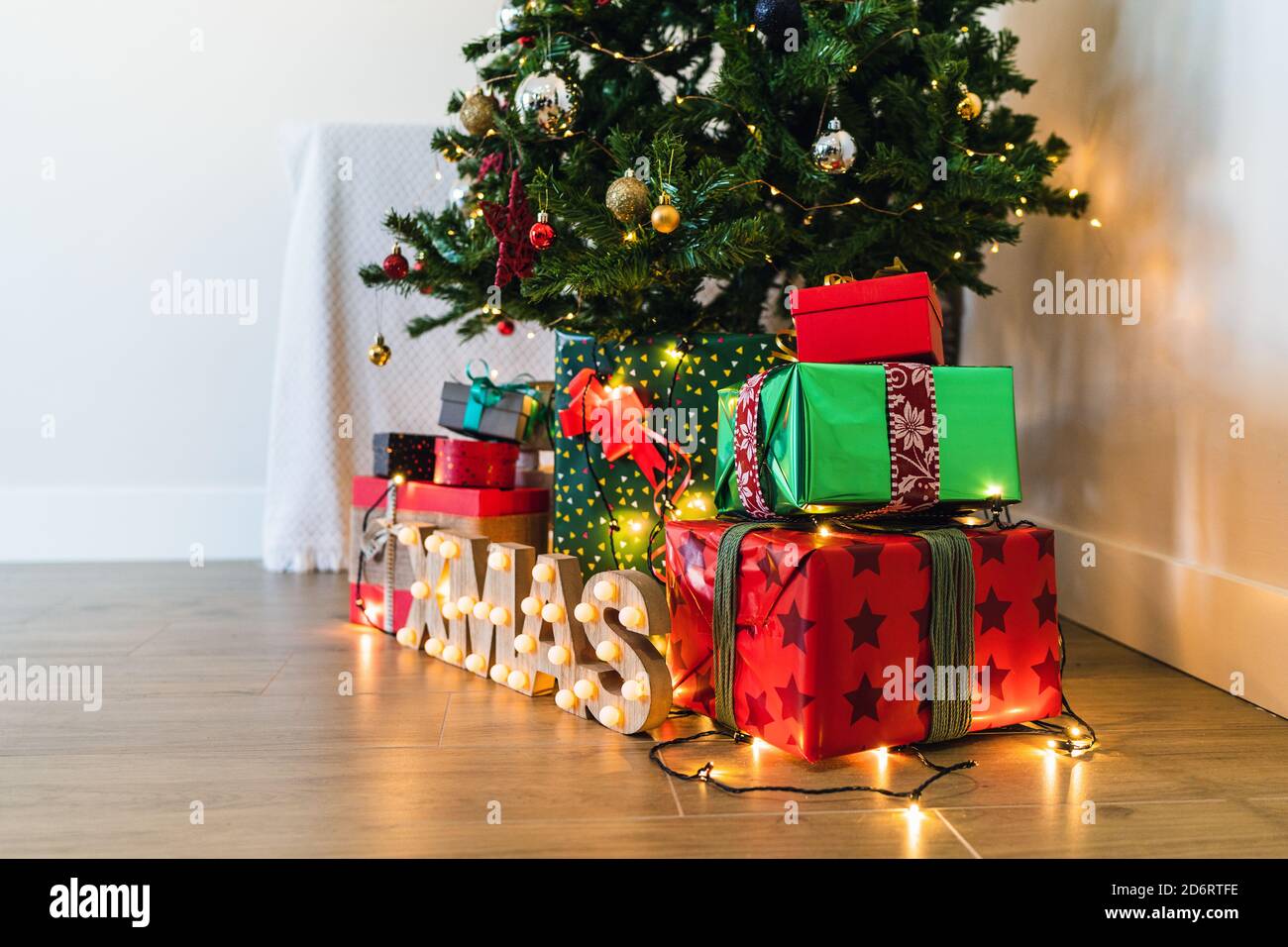 Haufen von bunten dekorativen Geschenk-Boxen mit Bändern in der Nähe dekorativ Pelzbaum und glänzende Buchstaben auf dem Boden mit Girlande während Festliche Veranstaltung Stockfoto
