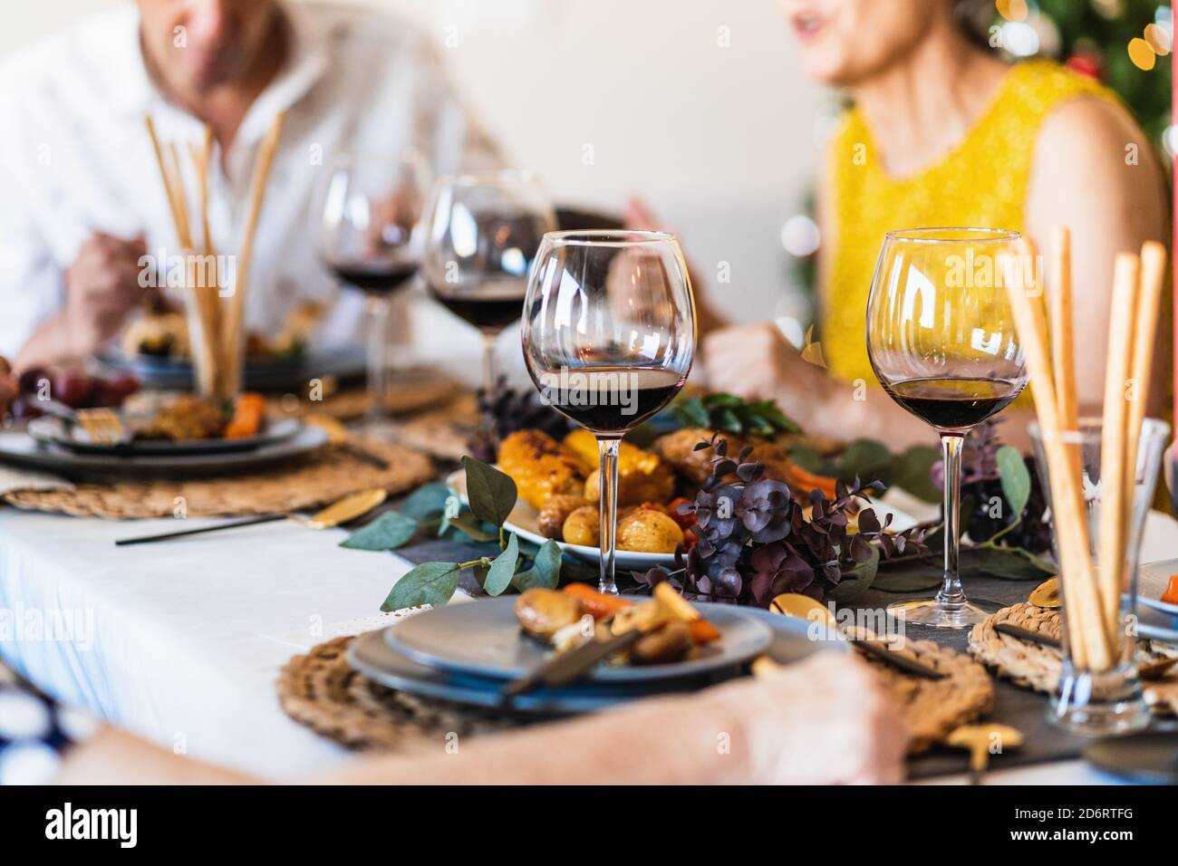 Esstisch serviert mit Gläsern und Tellern gegen verschwommenes Leuchten Weihnachtsbaum am Heiligabend zu Hause Stockfoto