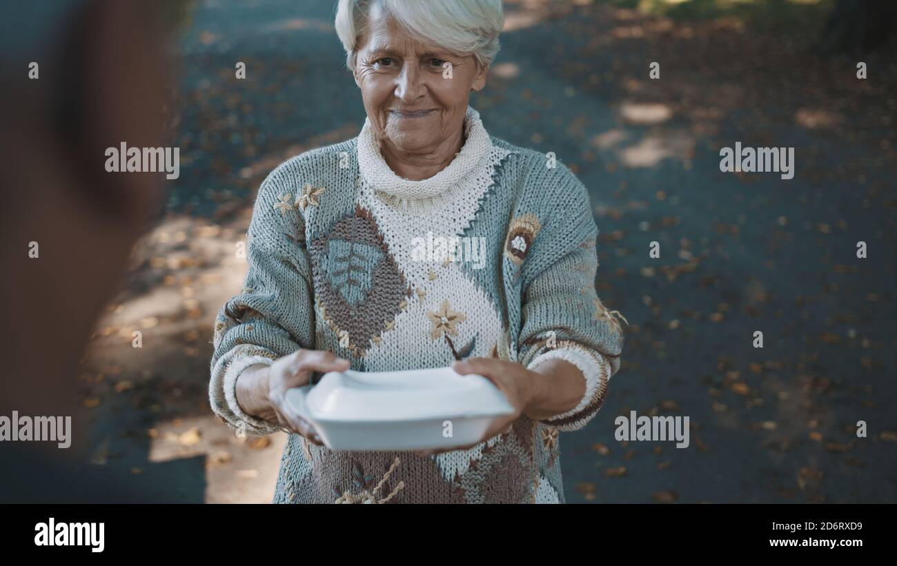 Alte schutzlose obdachlose Frau bekommt kostenlos Wohltätigkeitsessen. Hochwertige Fotos Stockfoto