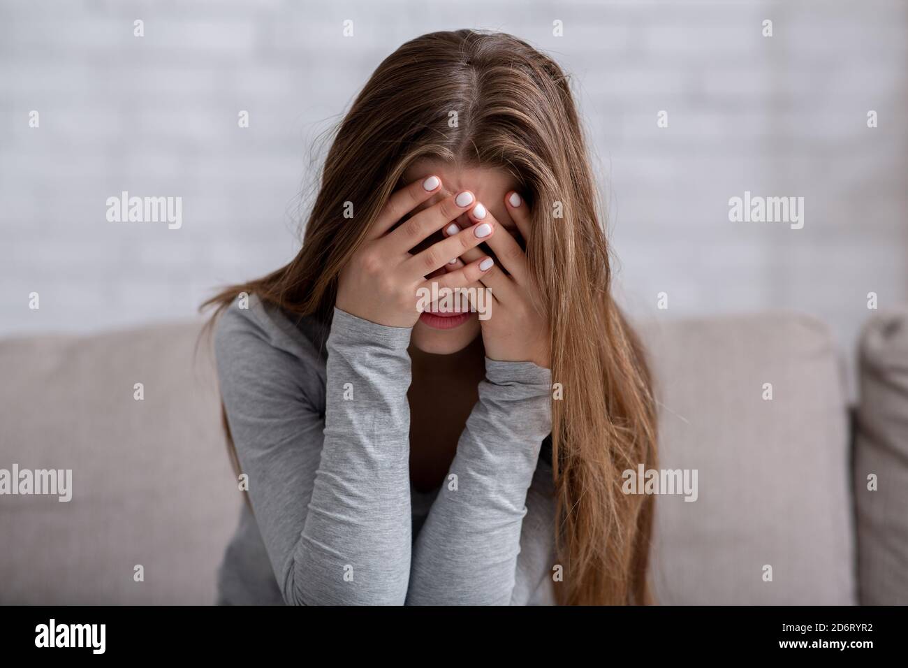 Millennial Frau, die ihr Gesicht mit Händen bedeckt und weint, depressiv oder gestresst fühlt Stockfoto
