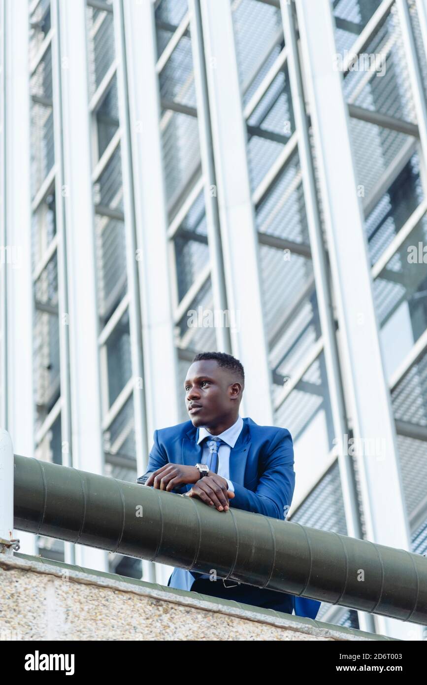 Niedriger Winkel der zuversichtlich respektablen afroamerikanischen Geschäftsmann in formellen Die moderne Innenstadtlage ist mit modernen Gebäuden und einer Straße verbunden Stockfoto