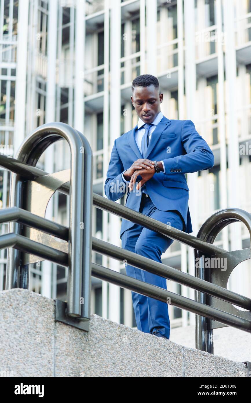Niedriger Winkel der zuversichtlich respektablen afroamerikanischen Geschäftsmann in formellen Die moderne Innenstadtlage ist mit modernen Gebäuden und einer Straße verbunden c Stockfoto