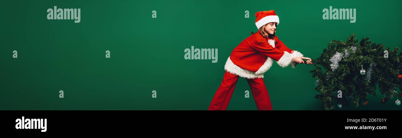 Mädchen in santa claus Kleid ziehen einen Weihnachtsbaum für die Einrichtung. Mädchen gekleidet als Santa Claus, ein Weihnachtsbaum. Stockfoto