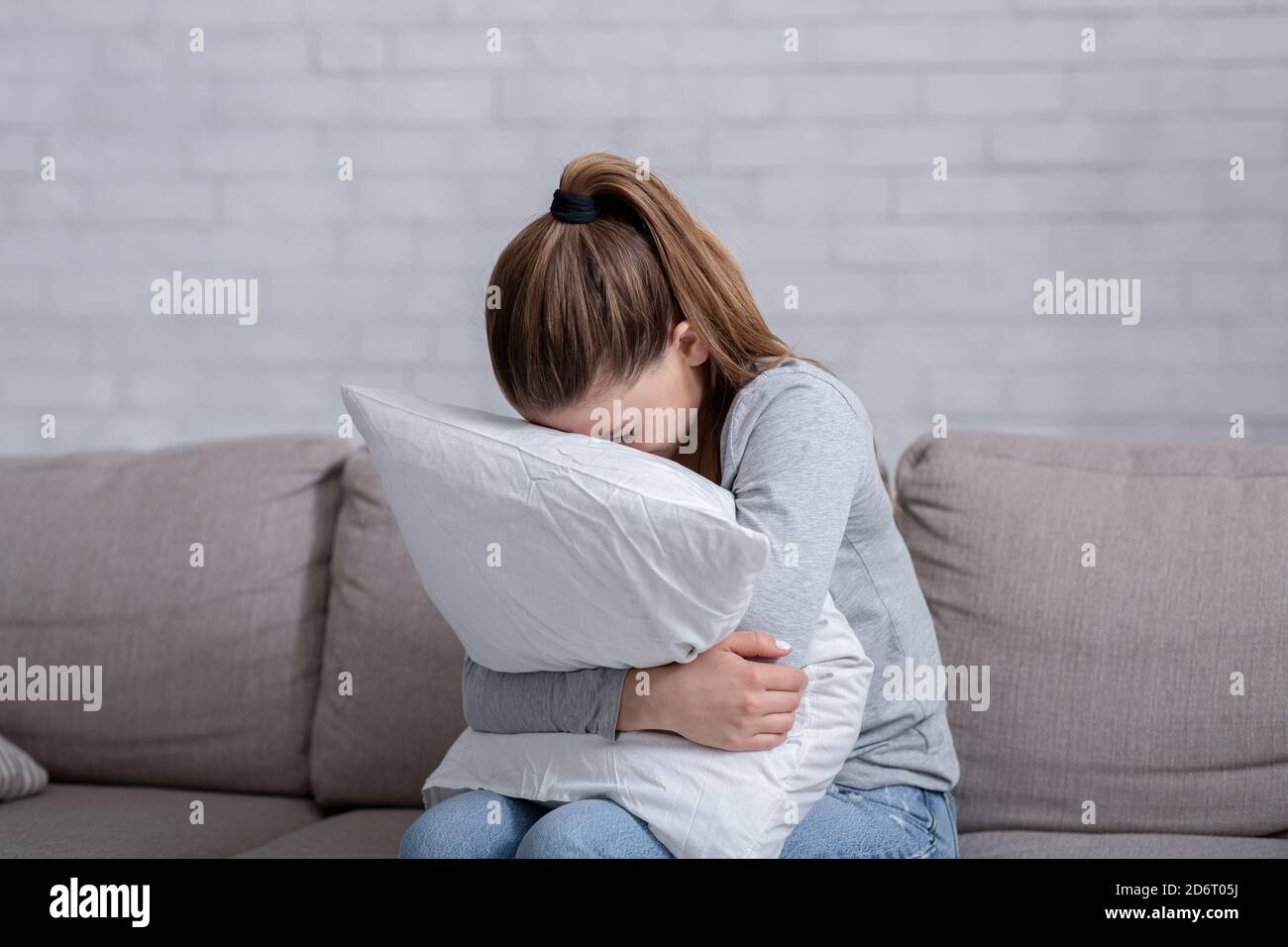 Junge Frau mit Depression umarmt Kissen und Weinen auf dem Sofa Zu Hause Stockfoto