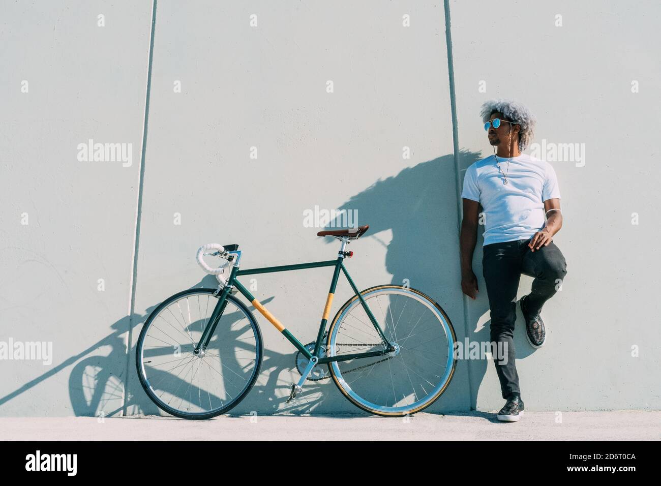 Schwarzer Radfahrer lehnt sich an eine graue Wand neben seinem Stadtrad. Black Rider Konzept. Afro-Radfahrer. Stockfoto