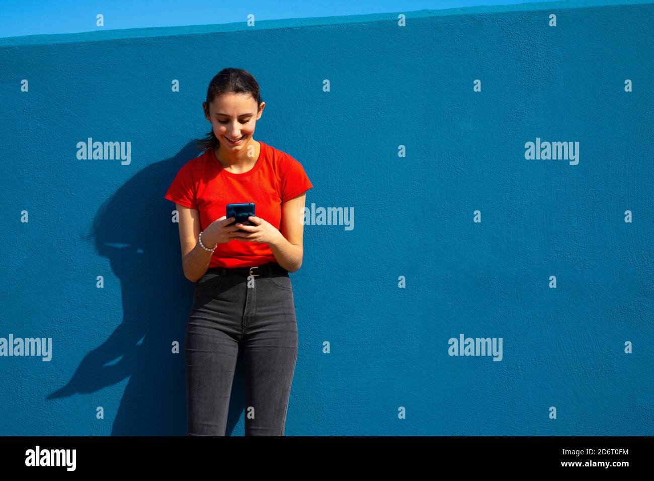 Frau in rot gekleidet mit dem Handy auf blauem Hintergrund. Konzept der Nutzung des Mobils. Blauer Hintergrund. Stockfoto