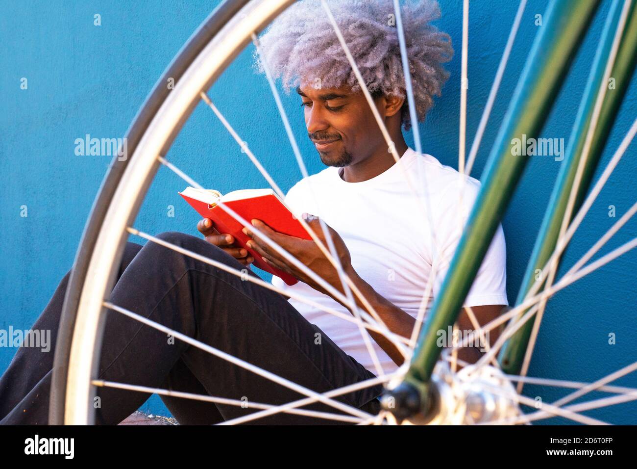 Schwarz und afro Mann liest ein Buch neben seinem Fahrrad. Konzept des schwarzen Mannes, der ein Buch liest. Stockfoto