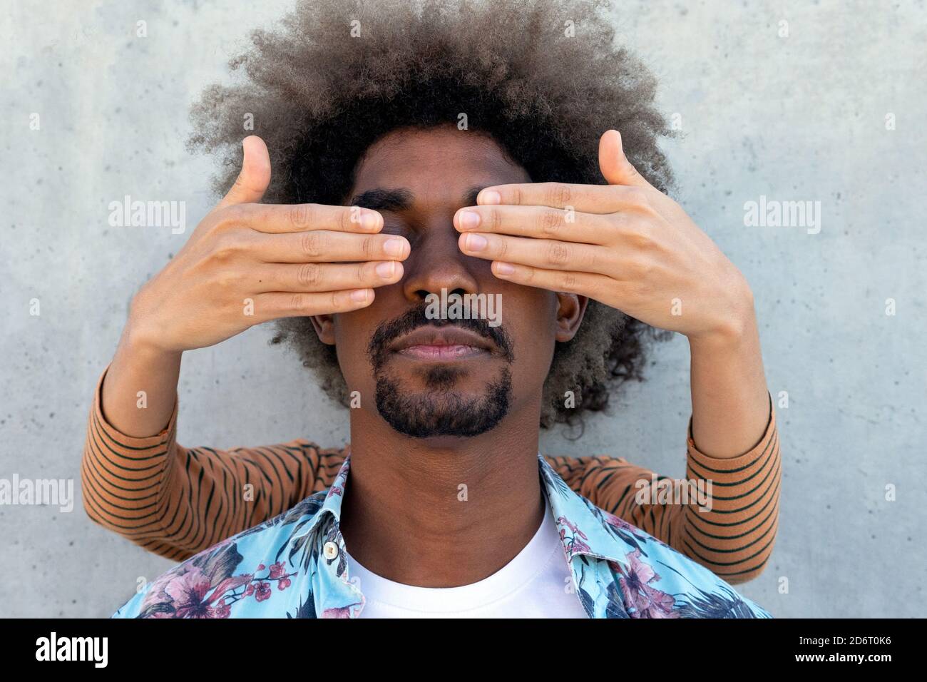 Anonymer Freund, der die Augen eines stylischen ethnischen Mannes mit Afro bedeckt Frisur in der Nähe Betonwand Stockfoto