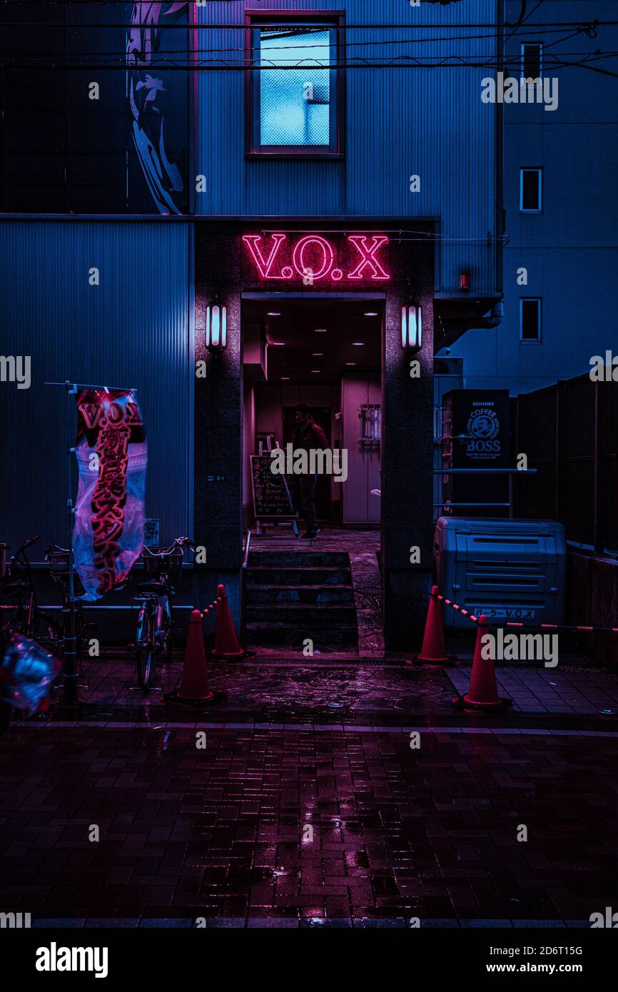 OSAKA, JAPAN - 27. Jan 2020: Ein Neonlicht über einer Tür beleuchtet die nasse Straße in einem violetten Licht. Stockfoto