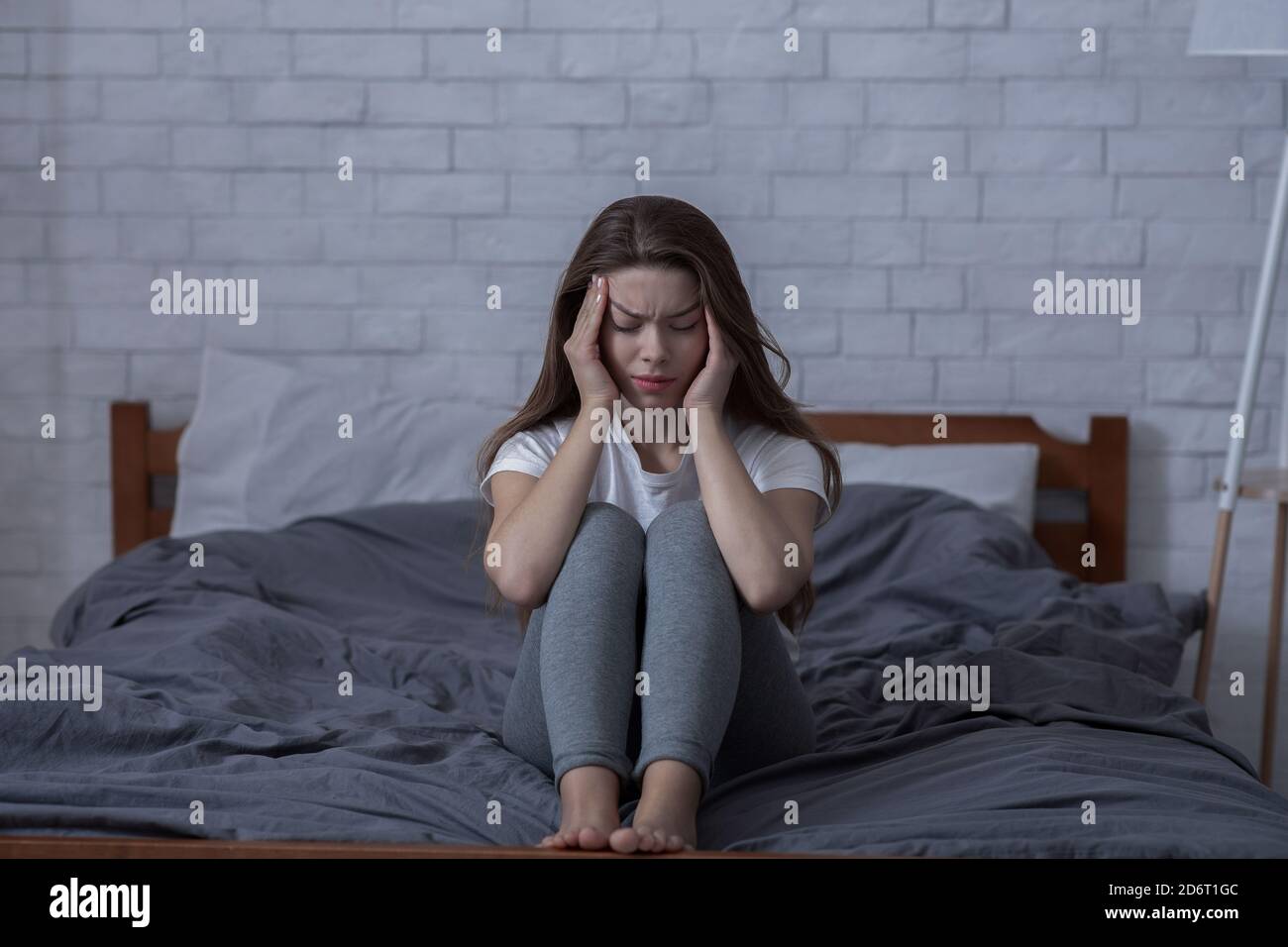 Negative Emotionen und psychische Gesundheit Konzept. Einsame junge Frau fühlt sich deprimiert, sitzt Kopf in den Händen im Schlafzimmer Stockfoto