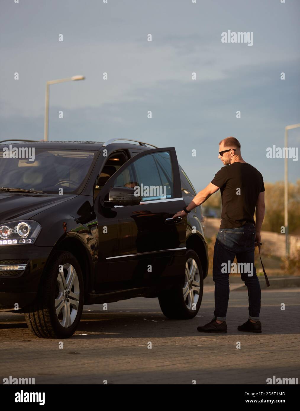 Gut aussehende sportliche Geschäftsmann lässig gekleidet öffnet die Tür seines coolen Autos auf der Straße, Seitenansicht, voller Länge, Kopierer Raum Stockfoto