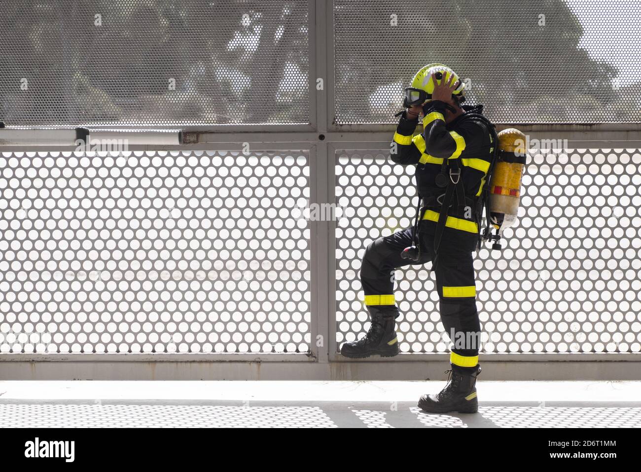 Seitenansicht der unrasierten Feuerwehrmann in bunten Uniform Anziehen hardhat beim Stehen mit Feuerlöscher in der Nähe von Gitter Zaun und Wegschauen Stockfoto