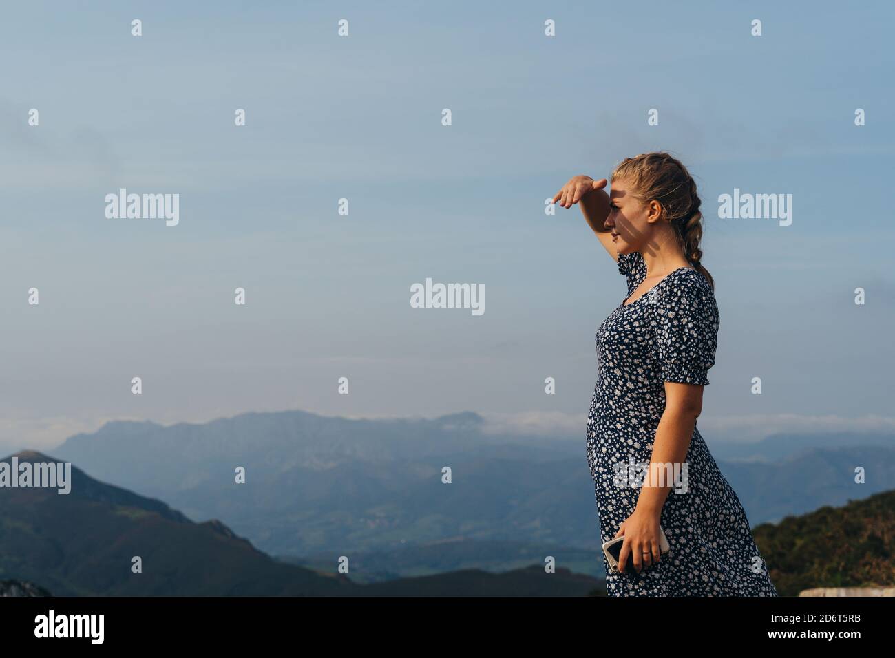 Seitenansicht positive junge Hündin mit Geflecht, das auf einem Hügel steht Und genießen Sie die malerische Landschaft der nebligen Hochland Stockfoto