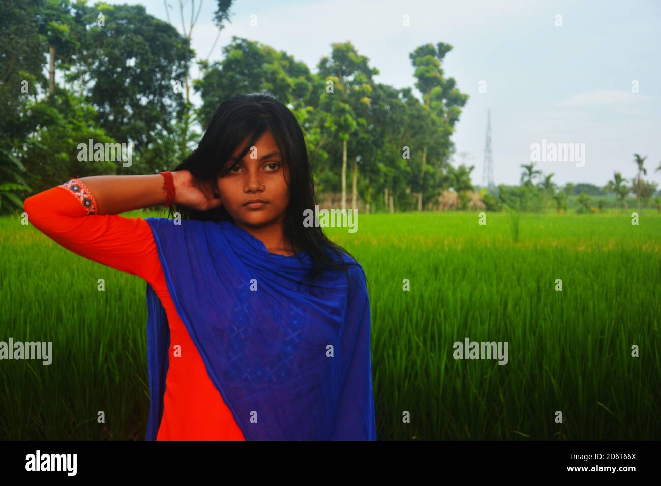 Nahaufnahme eines Teenagers, das Salwar Kameez und blaue dhupatta mit der rechten Hand am Hals trägt, auf einem Reisfeld stehend, selektiv fokussiert Stockfoto