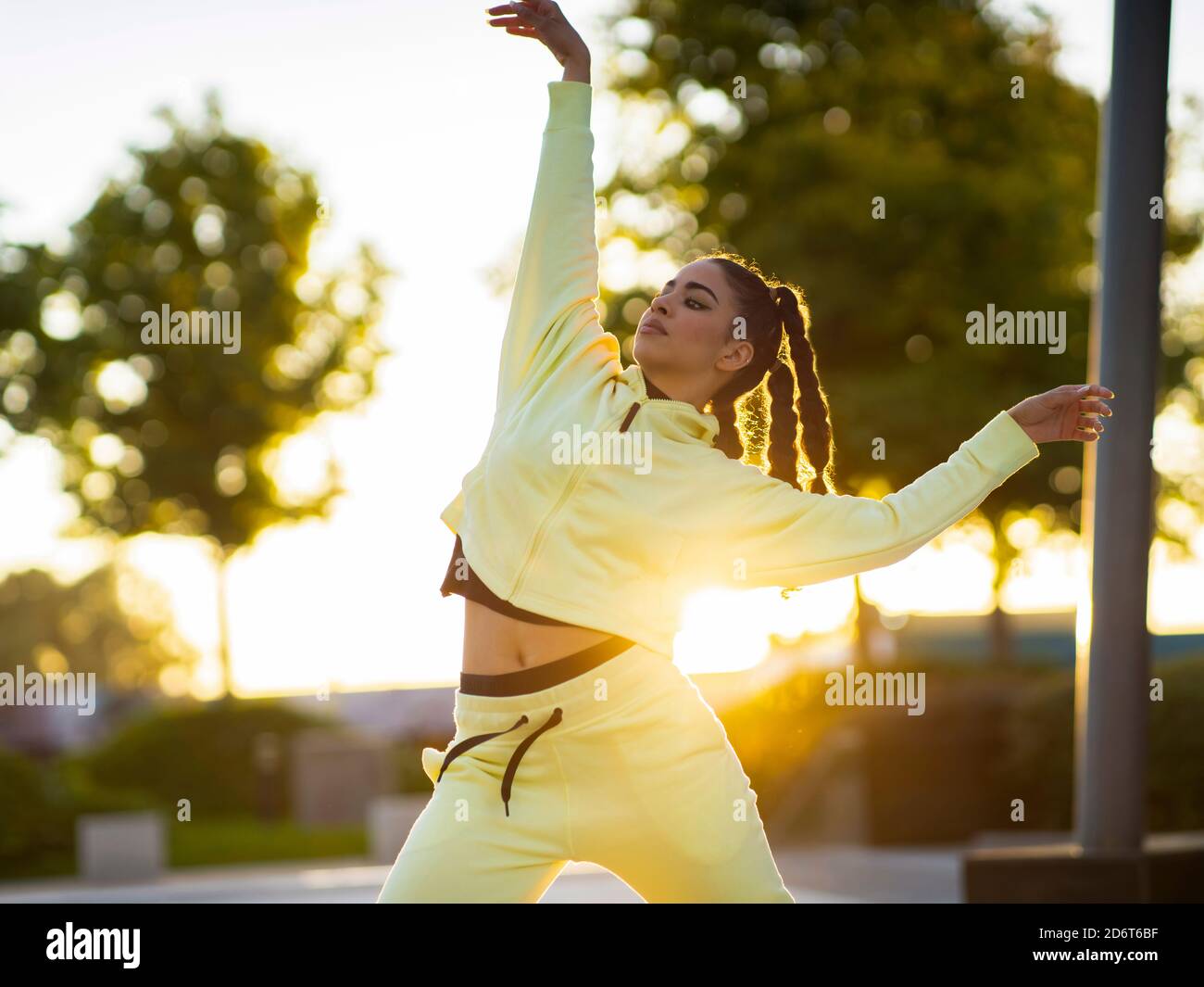 Trendige junge ethnische Tänzerin mit stilvoller Frisur in activewear Durchführung von Freestyle-Bewegungen im Park bei Sonnenuntergang Stockfoto
