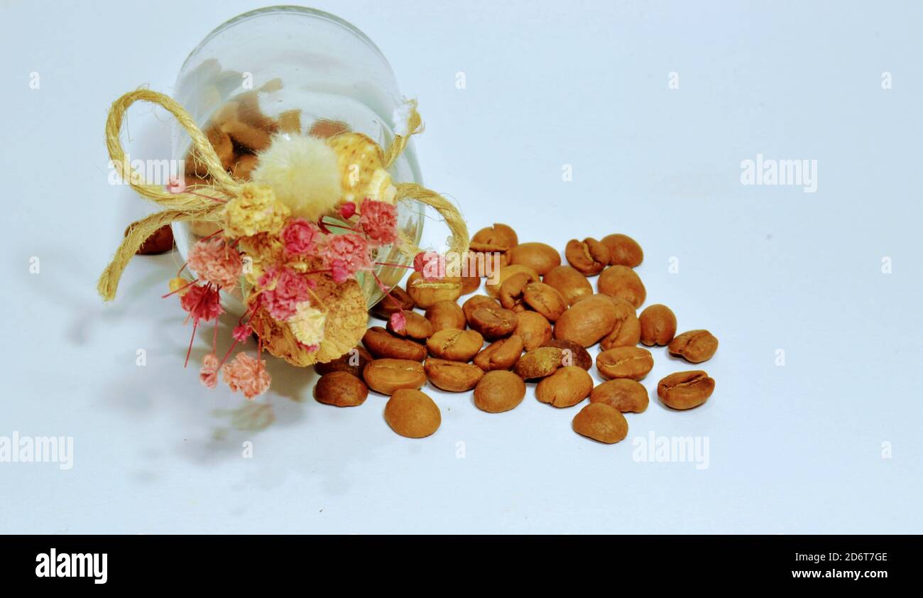 Frische und getrocknete Kaffeebohnen auf dem isolierten Hintergrund. Niedliche und kleine Glas und alten Stil Weinstopper mit künstlichen Blumen. Stockfoto